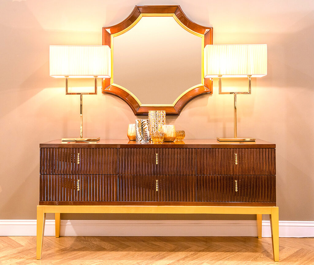 Buffet enfilade en bois massif sur pieds dorés surmonté de deux lampes design décoratives et d'un miroir hexagonal