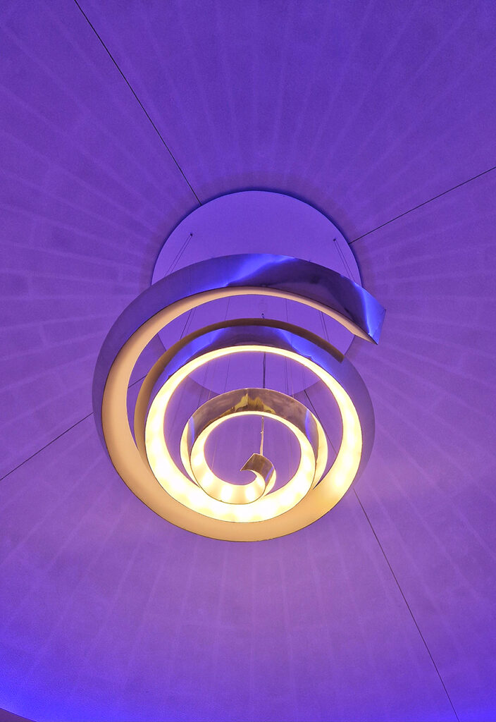 Lustre moderne en métal spiralé doré suspendu à un plafond violet, diffusant des reflets lumineux artistiques