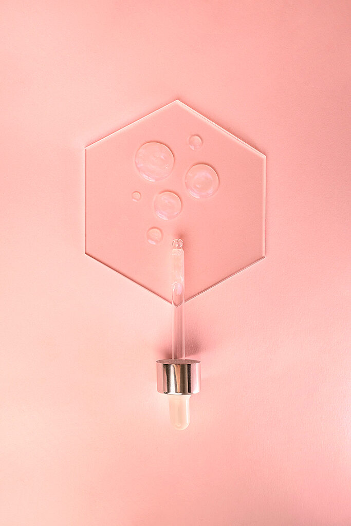 Gros plan sur des gouttes de sérum translucide sur fond rose délicat