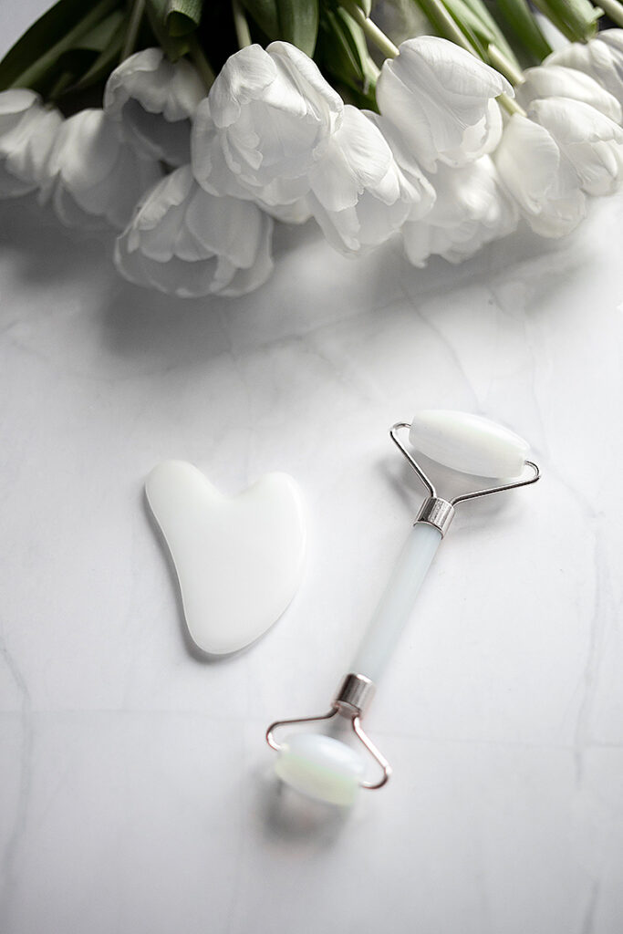 Rouleau et gua sha en quartz blanc pour massage du visage et bouquet de tulipes blanches