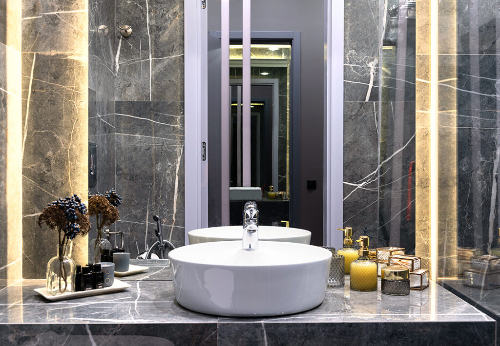 Salle de bains luxueuse avec produits cosmétiques, marbre et miroir rétroéclairé illustrant le luxe accessible par Élite Sélect.