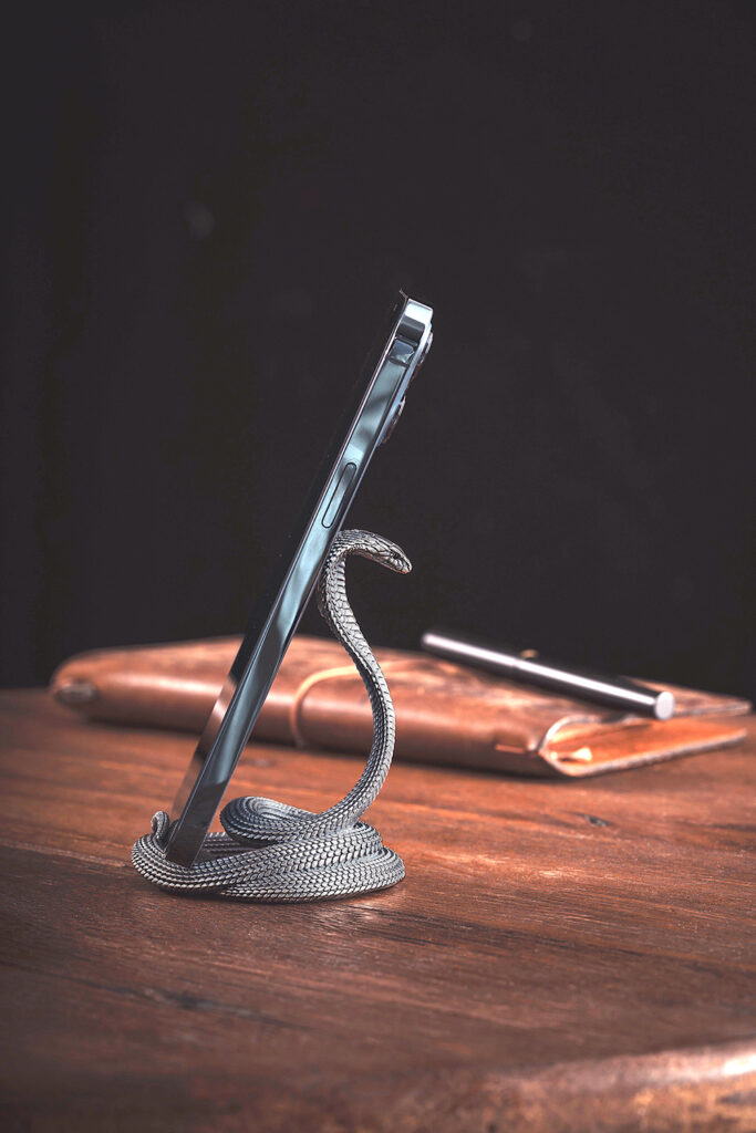 Support de bureau luxueux pour téléphone portable en forme de serpent, sur une table en bois précieux, à côté d'un carnet en cuir