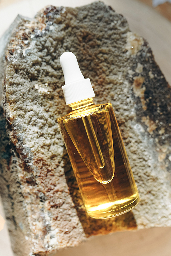 Flacon ambré minimaliste de sérum à la vitamine C posé sur une pierre grise texturée, ambiance haut de gamme style Vogue
