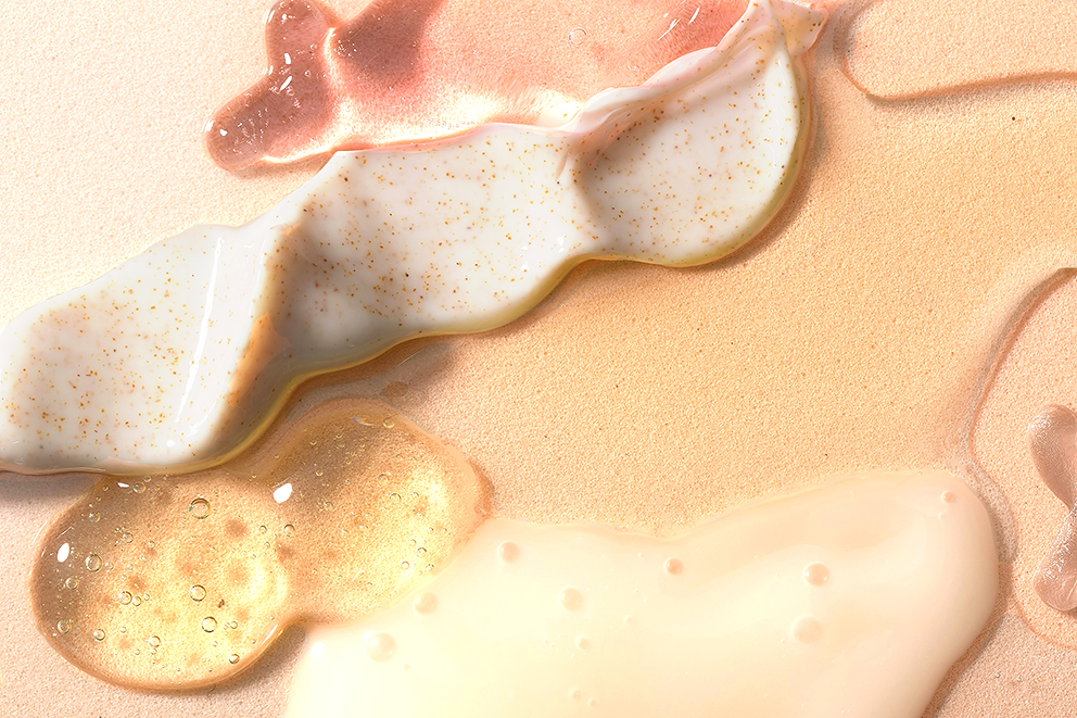Produits de soins de beauté de différentes textures et couleurs (sérum, crème, lotion) déposés sur un fond rose